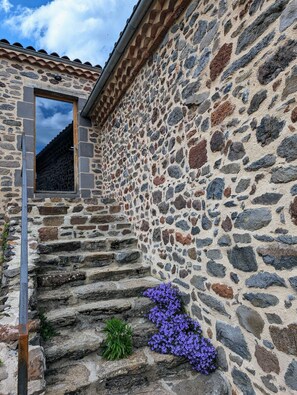 Una escalera de piedra conduce a un vano con una pequeña ventana, todo ello rodeado por un muro de piedra con tejado de tejas.