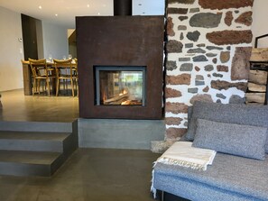 Una sala moderna con pared de piedra, chimenea, un sofá y un comedor al fondo.