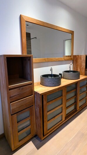 Un baño con tocador de madera, dos lavamanos redondos y un espejo grande.