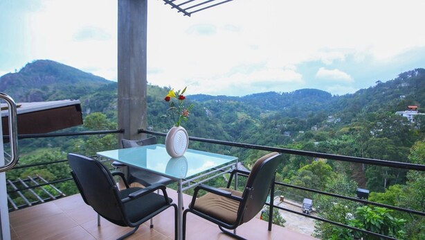 A balcony with a glass table and chairs, a vase with flowers, and a view of a green valley with hills. - Ella Floating View (Ella)