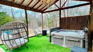 An outdoor patio with artificial grass, a hot tub, wicker furniture, and a hanging chair. - The Oasis - a shabby-chic, glamping escape to the wild side at Oak Meadow Ranch (Valley View)