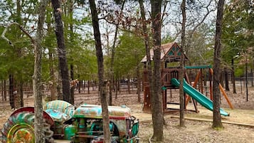 A playground with a slide and a playhouse, surrounded by trees.