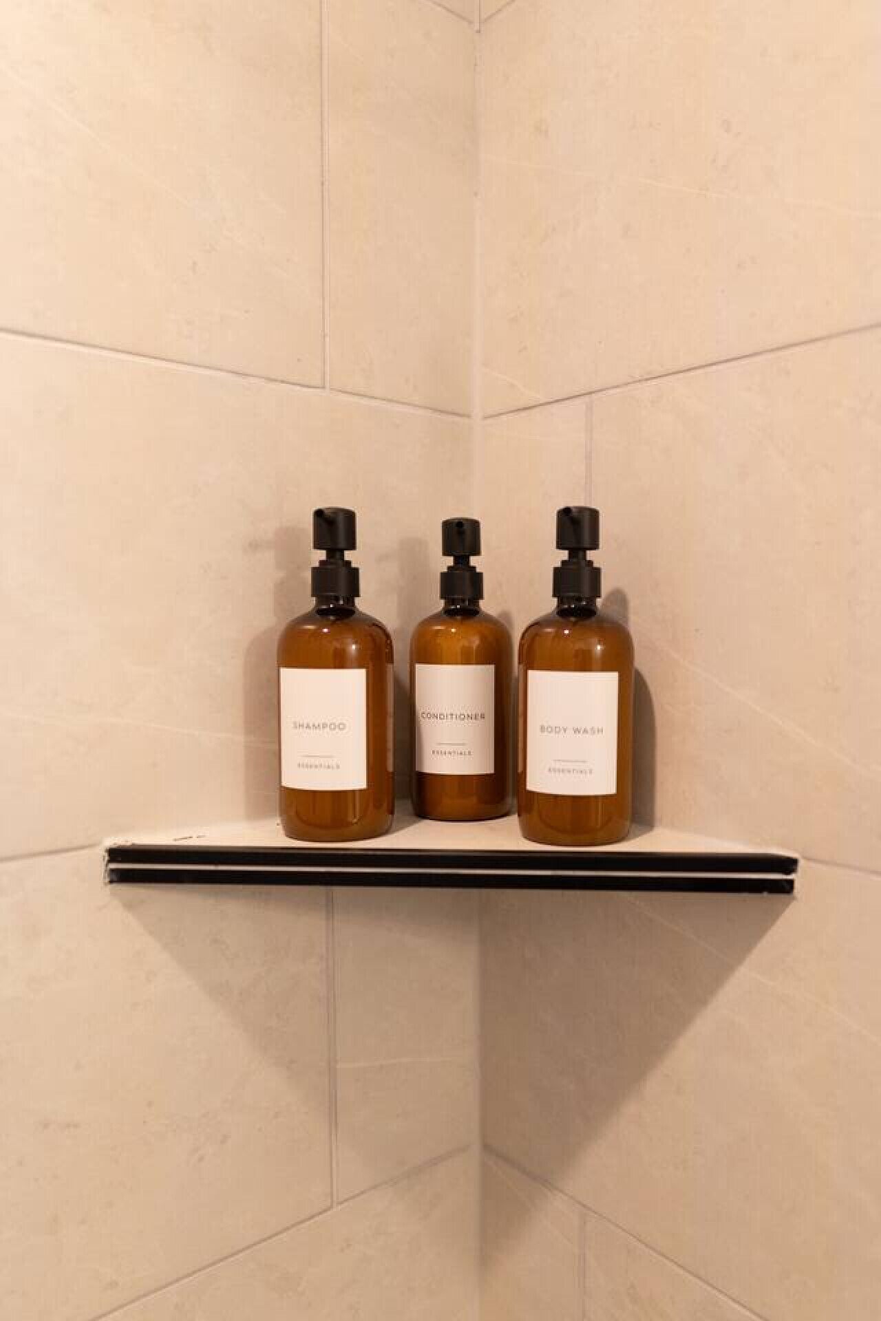 Three bottles of shampoo, conditioner, and body wash on a shelf in a bathroom.