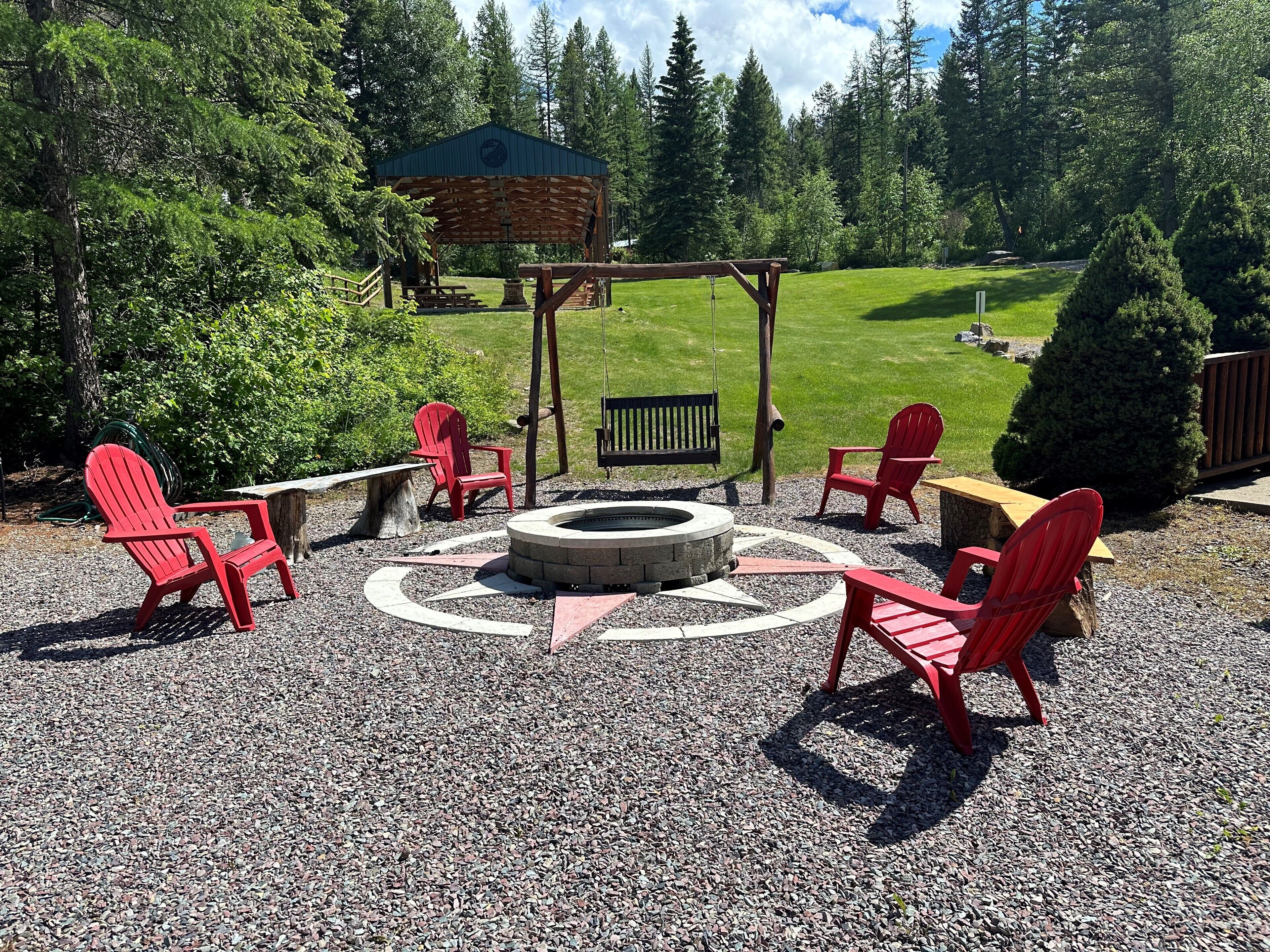 Un espace extérieur abrité avec des chaises Adirondack rouges, un foyer et un banc en bois.
