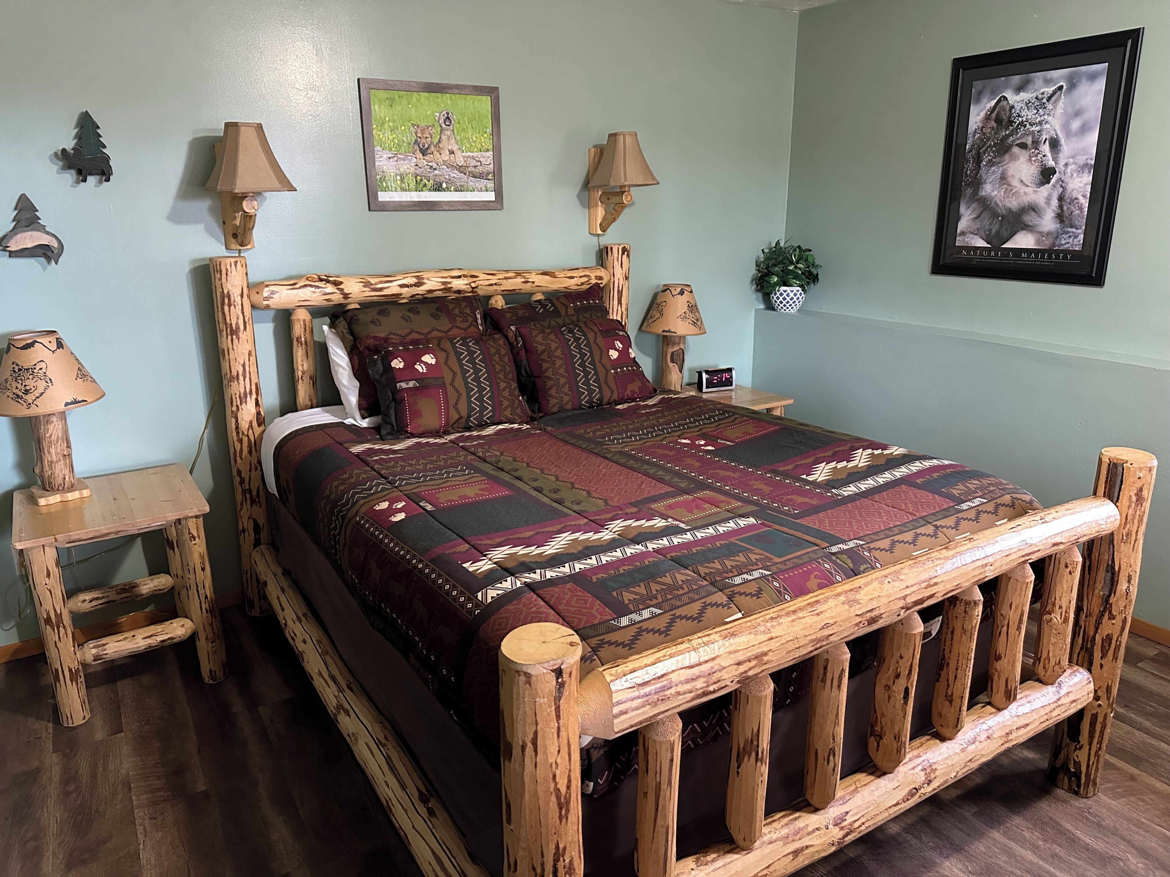 Un lit en bois rustique, surmonté d’une couvre-lit à motifs, deux tables de chevet avec des lampes et un tableau encadré accroché au mur.