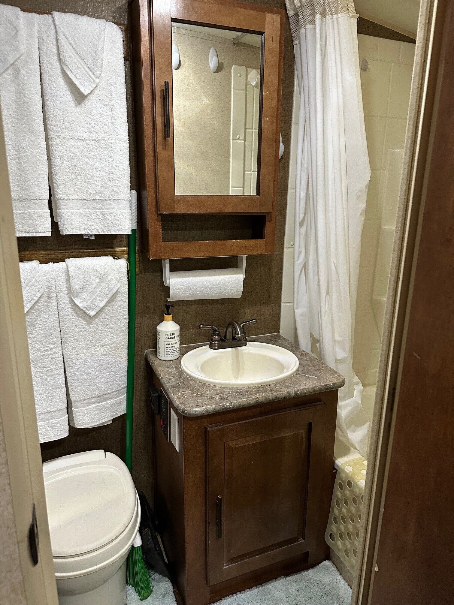 A bathroom with a sink, mirror, and toilet. There are towels hanging on the wall and a shower curtain.