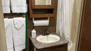 A bathroom with a sink, mirror, and toilet. There are towels hanging on the wall and a shower curtain.