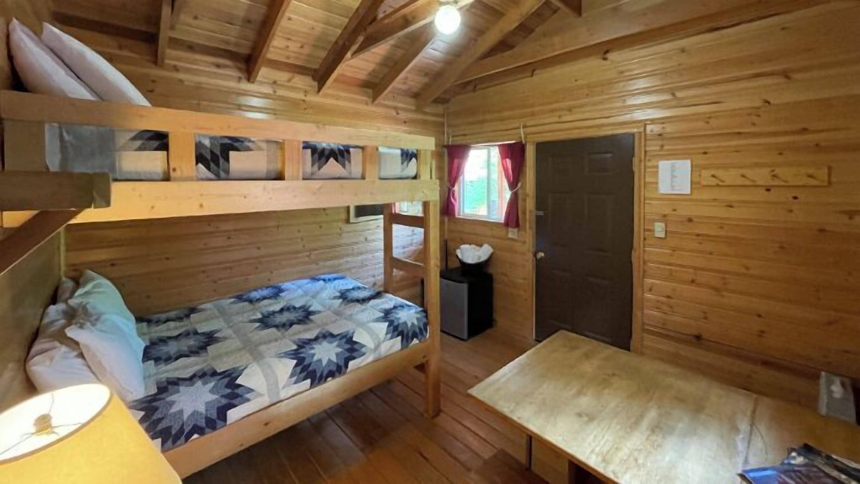 Une cabane en bois avec un lit superposé, une petite table et une porte.