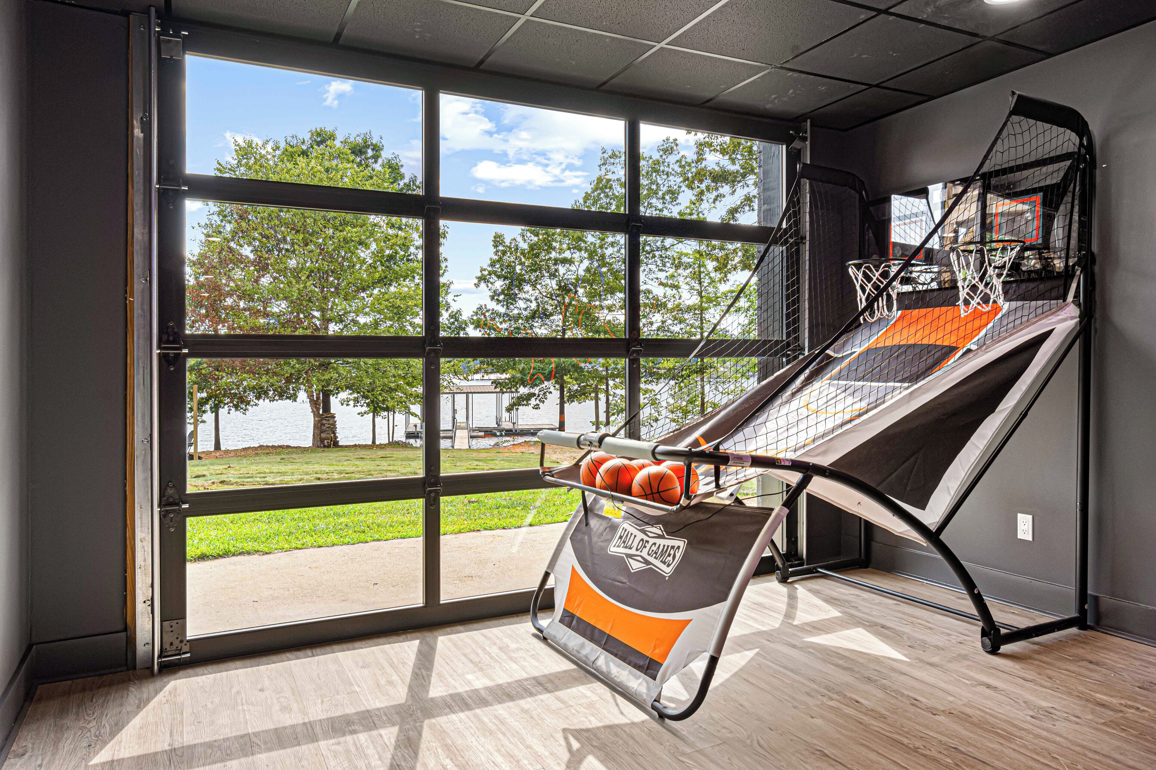 A basketball hoop with a net and backboard, a basketball, and a "Hall of Games" banner, all in a room with large windows and a view of a park.