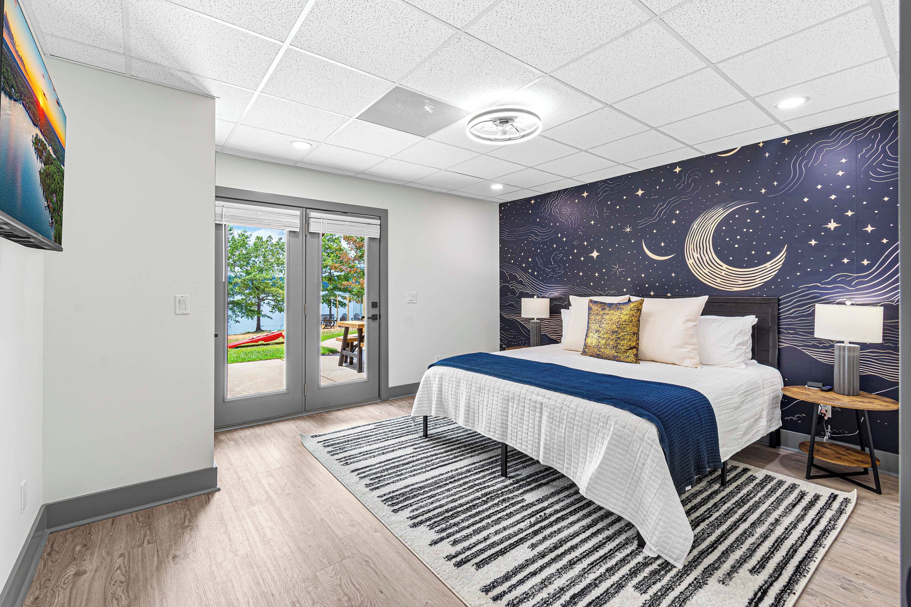 Ein modernes Schlafzimmer mit Bett, Wandmalerei mit Nachtlandschaft und Blick ins Freie.