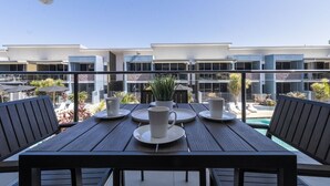 Eine Terrasse mit einem Tisch für vier Personen, mit Blick auf einen Pool und ein Gebäude mit zahlreichen Fenstern.