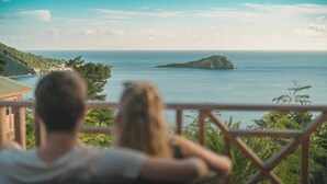 Una pareja sentada en un balcón con vistas a la costa y una isla distante.