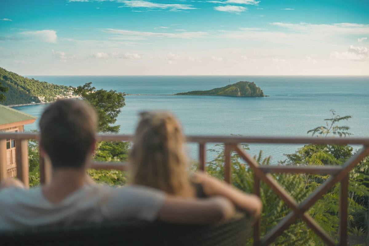 A couple sitting on a balcony overlooking a coastal view with a distant island.