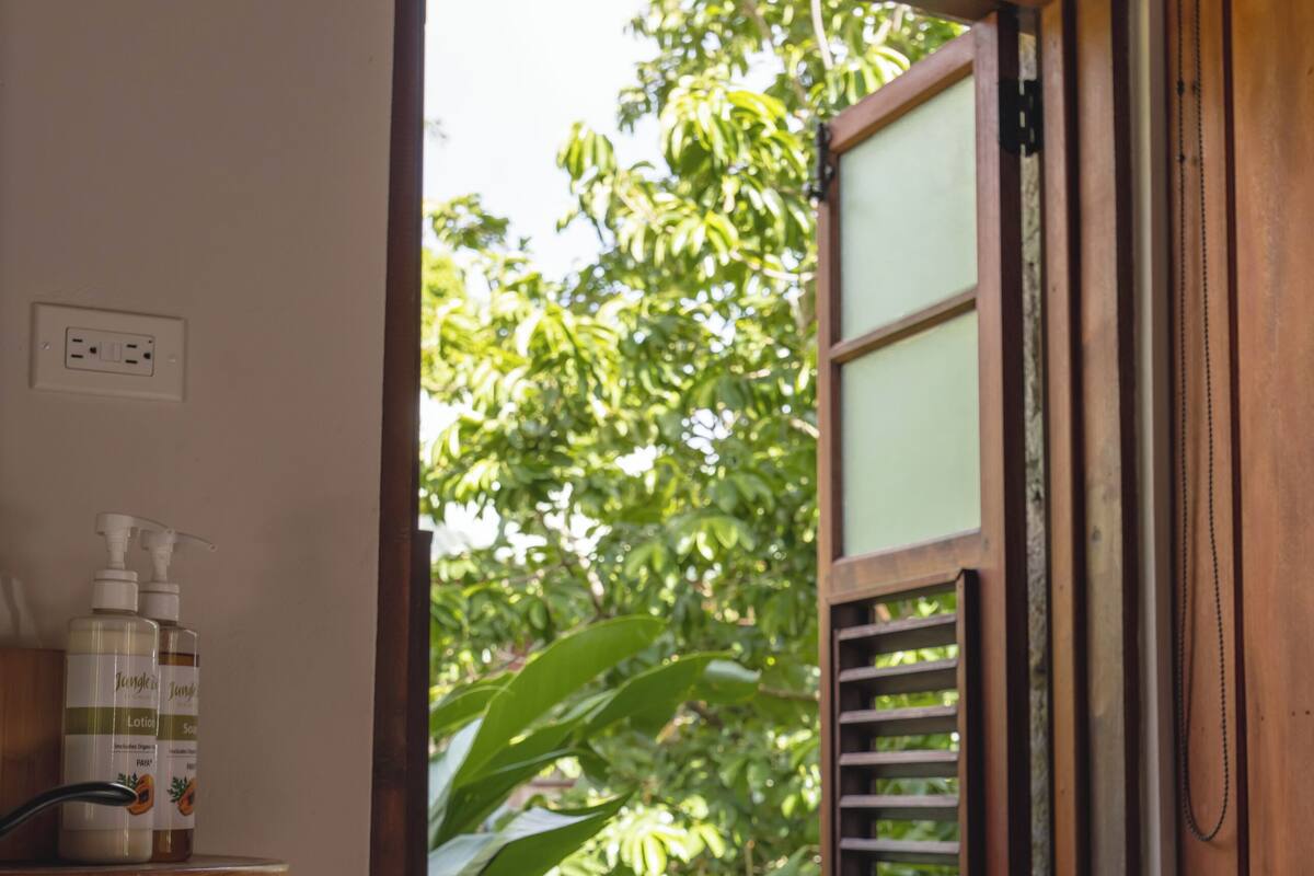 A bathroom with a stone sink, wooden window frame, and a view of greenery outside.