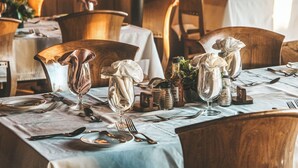 Un comedor con mesas y sillas de madera, manteles blancos y cristalería dispuesta para una comida.