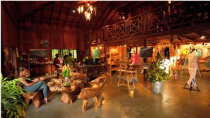 A rustic interior with wooden beams, a bar area, and a seating area with a unique wooden table centerpiece. - Jungle Bay Dominica (Soufriere)