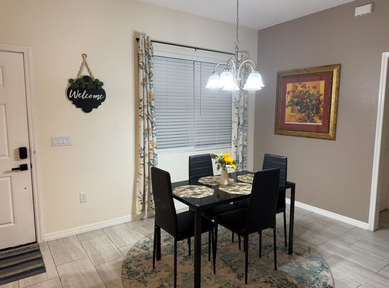 Un coin repas avec une table dressée pour quatre personnes, un lustre et un tableau accroché au mur.