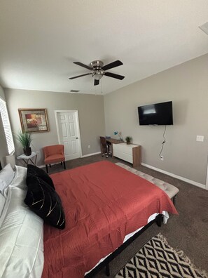 A bedroom with a bed, a desk, a chair, a television, and a ceiling fan.