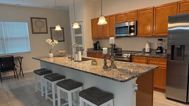 Una cocina moderna con encimeras de granito, electrodomésticos de acero inoxidable, armarios de madera y una zona de bar con taburetes.