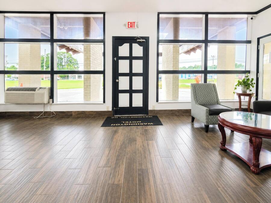 A hotel lobby with a reception desk, a waiting area with a chair, a coffee table, and large windows offering a view of the outside.