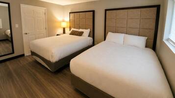 A hotel room with two beds, a door, a mirror, and a nightstand with a lamp.