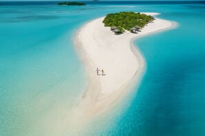 An aerial view of a secluded beach with a small island, clear turquoise waters, and a couple walking along the shore. - Nest by Hawks Hotels Kamadhoo Baa Atoll (Kamadhoo)