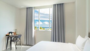 A hotel room with a large bed, a desk with a chair, and a view of the sea through a window with curtains. - Nest by Hawks Hotels Kamadhoo Baa Atoll (Kamadhoo)