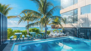 A pool area with lounge chairs and tables, palm trees, and a view of the ocean. - Nest by Hawks Hotels Kamadhoo Baa Atoll (Kamadhoo)