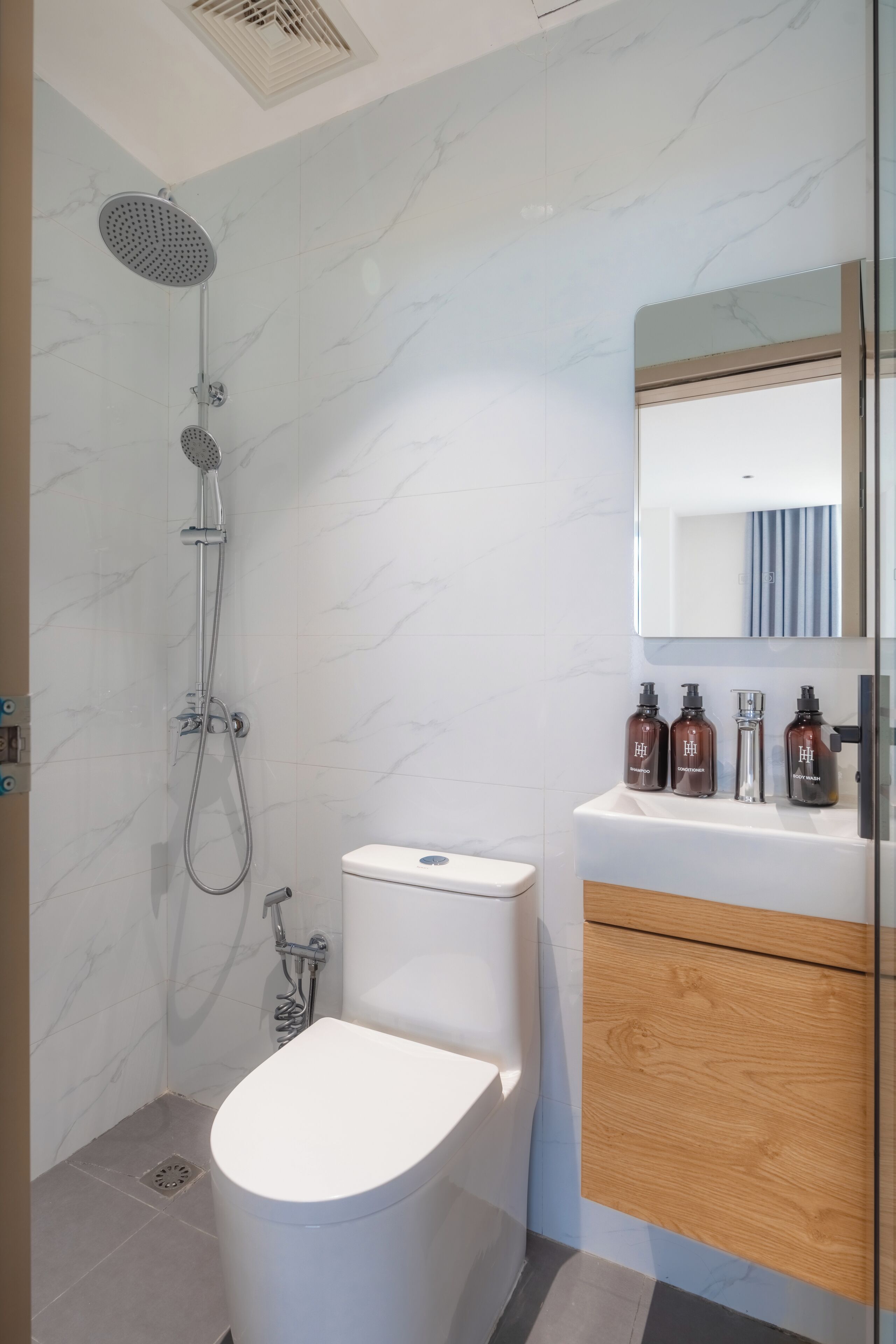 A modern bathroom with a shower, toilet, vanity, and a mirror.
