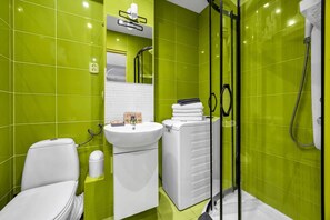 Een badkamer met groene tegels, een wit wastafelmeubel, een toilet en een douchehoek.