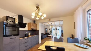 A modern kitchen with a built-in oven and microwave, a dining area with a wooden table and chairs, and a living room with a sofa and coffee table. - Tammen's "Klönstuv" - stylish & cozy (Papenburg)