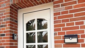 A white door with six glass panes, a white mailbox, and a doorbell on a brick wall. - Tammen's "Klönstuv" - stylish & cozy (Papenburg)
