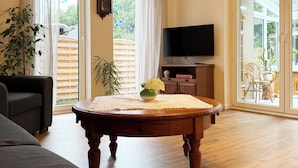 A spacious living room with a wooden floor, a sofa, a coffee table with a vase, a flat-screen TV, and a sliding glass door leading to an outdoor area. - Tammen's "Klönstuv" - stylish & cozy (Papenburg)