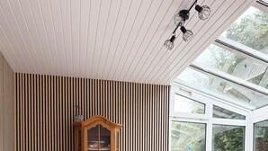 A room with two wicker chairs, a wooden cabinet with glass doors, and a large window with a view of greenery. - Tammen's "Klönstuv" - stylish & cozy (Papenburg)
