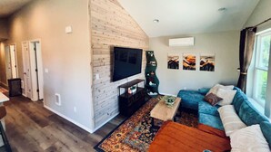 Un salon moderne avec un téléviseur fixé sur un mur en bois, un canapé bleu, un tapis à motifs et une petite table agrémentée d’objets décoratifs.