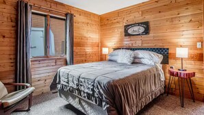 Ein Zimmer mit Holzwänden, einem Bett, einem Sessel, einem Tisch mit Lampe und einem Schild an der Wand.