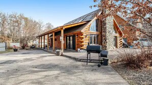 Eine Blockhütte mit Steinverkleidung, einer Veranda und einem Grill vor der Tür.