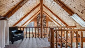 Ein Zimmer mit hohen Holzbalken und einer Steinsäule, ein schwarzer Ledersessel und Blick ins Freie.