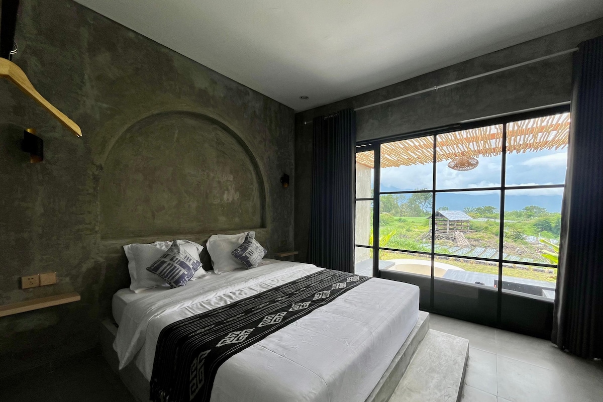 Ein Schlafzimmer mit einem großen Bett, Blick auf eine Landschaft und einer Betonwand.