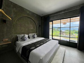 Ein Schlafzimmer mit einem großen Bett, Blick auf eine Landschaft und einer Betonwand.