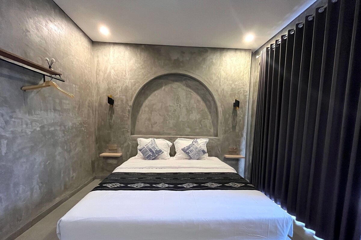 Ein modernes Schlafzimmer mit einem großen Bett, einem Holzregal und einem dunklen Vorhang.