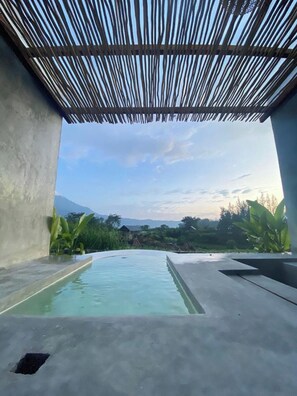 Ein Pool mit Blick auf Berge und Grünflächen, eine Betonkonstruktion und eine Bambusdecke.