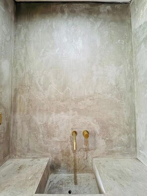 Ein Badezimmer mit strukturierter Wand, einem rechteckigen Waschbecken und zwei goldenen Wasserhähnen.