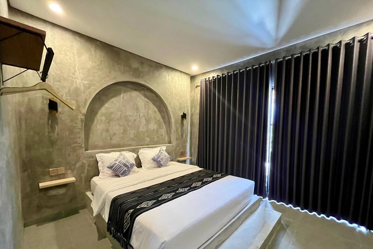 A modern bedroom with a large bed, a headboard, a bedside table, and a window with curtains.