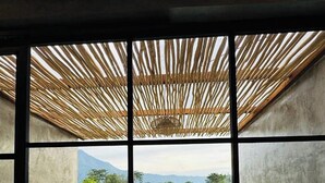 A room with a concrete floor, a window with a bamboo ceiling, and a view of a green landscape with fields and a small building. - Batur Sunsun Kintamani By Zuzu (Kintamani)