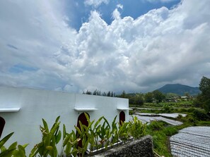 A building with a flat roof, a red door, and a view of terraced fields and mountains in the background.