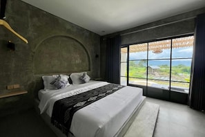 Une chambre avec un grand lit, une vue sur la verdure et un mur en béton.