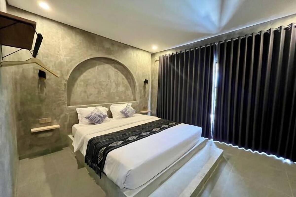 A bedroom with a bed, a nightstand, a wall-mounted TV, and a window with curtains.