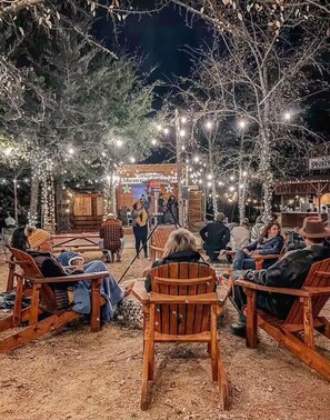 A rustic outdoor seating area with wooden chairs and tables, surrounded by trees and string lights. - The Paradise - glamp with us and explore the wild side at Oak Meadow Ranch! (Valley View)