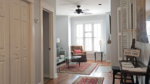 A spacious living room with hardwood floors, a ceiling fan, a red and beige patterned rug, a brown armchair with a red pillow, and a table with papers. - Charming Historic Grant Park Home / Atlanta Gem! (Atlanta)